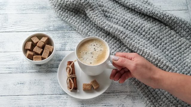 Female hand takes a coffee mug. Coffee mug, sweater, cinnamon,brown sugar. Cozy autumn composition. Hygge concept. 4K footage