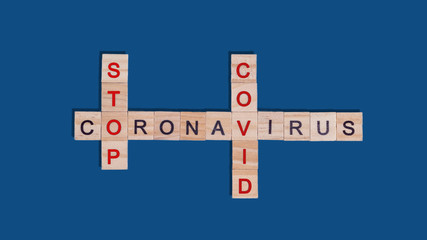 Text crossword puzzle of wooden red and black letters stop coronavirus covid on a blue classic background. Concept of ending quarantine, protection from spread of viral infection during a pandemic.