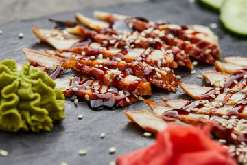 Smoked eel sliced fillet with fresh cucumber, pickled ginger and wasabi on slate plate
