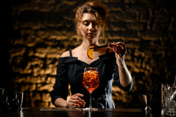 bartender girl decorates glass of cocktail with slice of citrus.