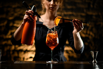 bartender girl decorates glass of cocktail with slice of citrus and pours carbonated drink.