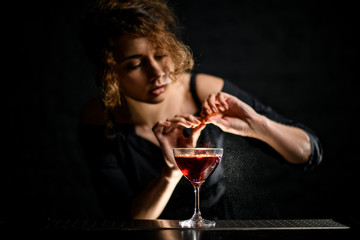 Woman bartender sprinkles citrus juice on beautiful glass with wine.