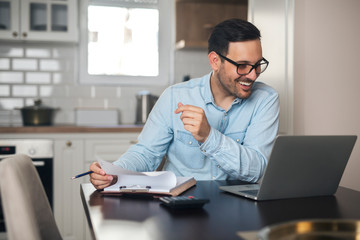 Young man doing paperwork and using laptop.