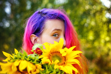 Pink and lilac strands of hair. A beautiful happy teenage girl with a sunflower enjoys nature and laughs on a summer field. The sun's glare, the sun's rays, the sun's radiance. Illuminated