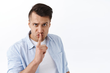 You better shut your mouth. Portrait of threatening serious pissed-off man, shushing at camera with index finger pressed to lips, frowning hush person be quiet, standing white background