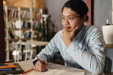 Image of pleased asian man studying and writing on exercise book