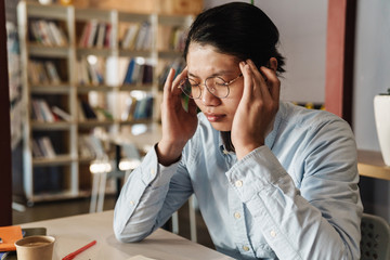 Image of tired asian man with headache rubbing his temples