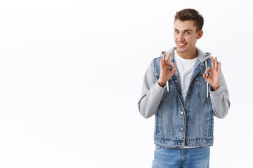 Portrait of handsome confident guy assuring in best quality of product, show okay signs and smiling, recommend promo offer, approve good plan, like something, agree on terms, white background