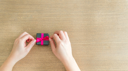 Mains faisant un noeud rose sur un cadeau posé sur une table en bois