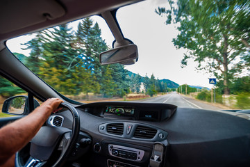 View of the road and landscape through the windshield of a passenger car, narrow road, speed can be seen on the speedometer, the driver is a man