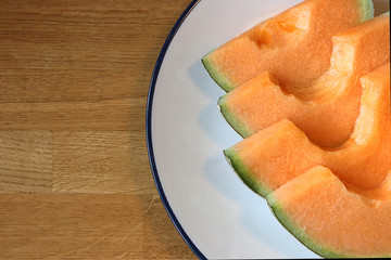 Close up sliced melons in white plate on wooden table.