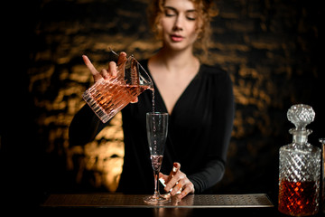 bartender girl pours ready-made cold cocktail from mixing cup into glass