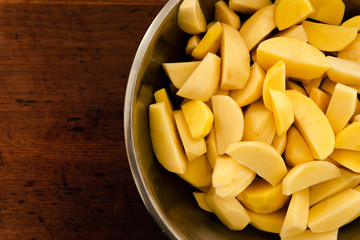 seasoned raw chopped potatoes,bowl of raw potatoes standing on the table,peeling potatoes for cooking,cooking baked potatoes,hand sprinkles seasoning in potatoes