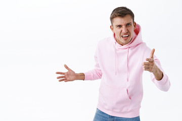 Portrait of angry, pissed-off blond man in pink hoodie, having argument, pointing finger at camera...