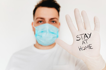 Stop Corona virus! A young european man in mask and gloves with sign Stay at home. Covid-19 protection