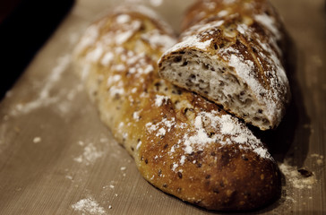 two baked homemade bread lie on the table,homemade baked bread with seeds,baguette sprinkled with flour,fresh bread on a black background,fresh bread texture