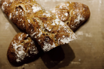 two baked homemade bread lie on the table,homemade baked bread with seeds,baguette sprinkled with flour,fresh bread on a black background,fresh bread texture