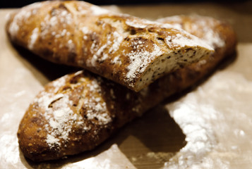 two baked homemade bread lie on the table,homemade baked bread with seeds,baguette sprinkled with flour,fresh bread on a black background,fresh bread texture