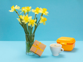 Bouquet of yellow daffodils in vase and a gift box on a blue background.