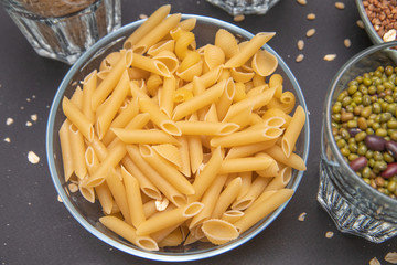 Close-up macaroni and other cereals in glass dishes stand on a gray background. Pearl barley. Beans. Buckwheat.  Vegetarian food. Source of protein and carbohydrates. Diet. Good nutrition. 