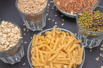 Macaroni and other cereals in glass containers stand on a gray background. Pearl barley. Beans. Mash. Red bean. Buckwheat. Vegetarian food. Diet. Good nutrition. Healthy food.