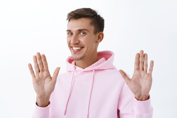 No thank you, I am okay. Portrait of handsome smiling blond man in pink hoodie, raising hands in...