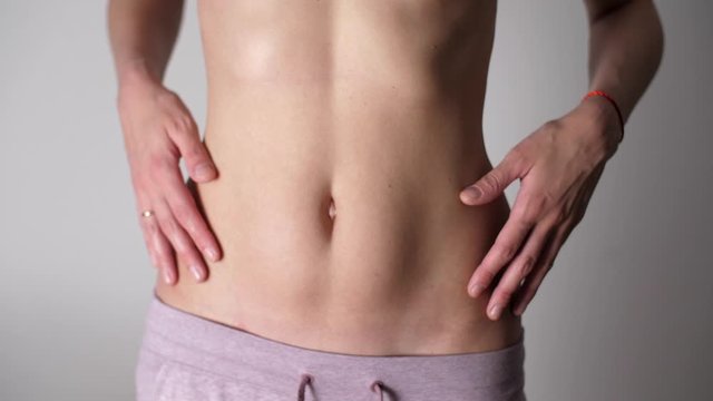 Girl touches her flat belly with her hands and retracts her stomach. White female's fit body and tan skin. Caucasian woman's flat stomach and arms. Weight Loss During Quarantine