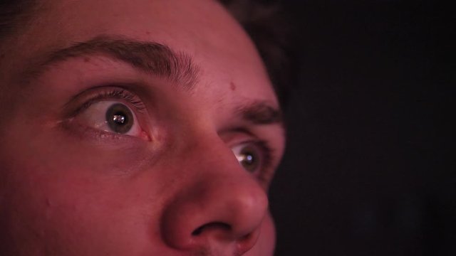 Close-up of a young man's eyes looking at screen in a deep night. Young man absorbed in video-games. Watching videos late night with exitement