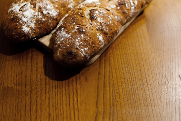 home baked fresh bread lying on a wooden table,two breads lie on a cutting board,branded home-baked bread,baguette with seeds,bran loaf