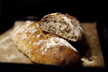 two baked homemade bread lie on the table,homemade baked bread with seeds,baguette sprinkled with flour,fresh bread on a black background,fresh bread texture