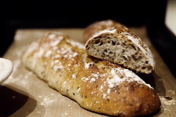 two baked homemade bread lie on the table,homemade baked bread with seeds,baguette sprinkled with flour,fresh bread on a black background,fresh bread texture