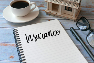 A cup of coffee,toy wooden house,glasses,pen and notebook written with Insurance. Concept of home insurance.