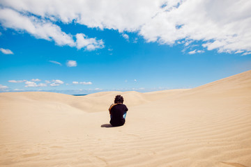 Man sit on a desert dune landscape. New experiences traveling around the world. Man sightseeing through the dunes in a warm summer day. Travel and holidays concept. Maspalomas natural landscape.