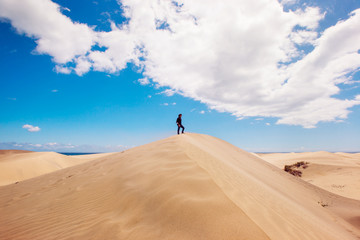 Panoramic landscape with man on the top of a desert dune. New experiences traveling around the world. Man enjoying freedom. Travel and holidays concept. Maspalomas natural landscape in Canary Island.