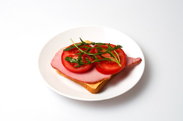 Sandwich of balyk, cheese, bread, tomatoes and arugula on a white plate on a plate