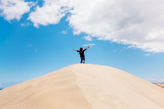 Unrecognizable man with arms wide open on the top of a desert dune. New experiences traveling around the world. Man enjoying freedom. Travel and holidays concept. Maspalomas natural landscape.