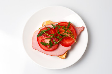 Sandwich of sturgeon, cheese, bread, tomatoes and arugula on a white background on a plate view from the top