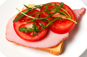 Sandwich of balyk, cheese, bread, tomatoes and arugula on a white plate on a plate flat lay