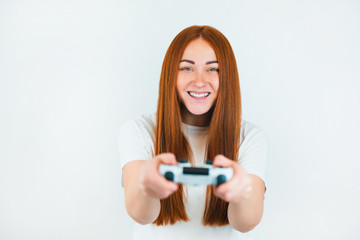 beautiful redheaded young women looks happy standing on isolated white backgroung playing online exciting game with joystick in her hands, leisure time spending concept