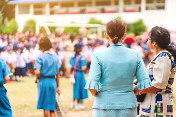 Asian female teacher stand to control the students playing music while lining up to pay respect to the national flag in the morning in school.