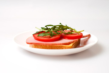 Sandwich of balyk, cheese, bread, tomatoes and arugula on a white plate on a plate view from the side