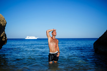 Happy man guy joy on vacation, stands at sea and splashes in the water. Men's shorts, sun, beach