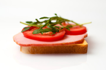 Sandwich made of balyk, cheese, bread, tomatoes and arugula on a white plate side view