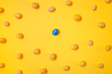One blue candy bean among yellow ones on bright yellow background. Social distancing, stay away concept.