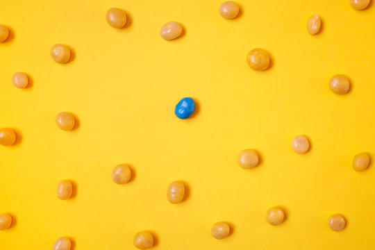 One blue candy bean among yellow ones on bright yellow background. Social distancing, stay away concept. - Powered by Adobe