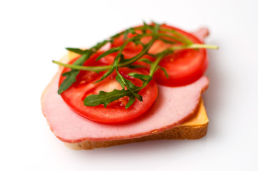 A sandwich of balyk, cheese, bread, tomatoes and arugula on a white plate view from the side and from the top