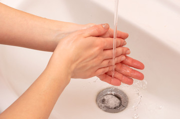 Young woman washes hands in the sink with soap. Warm tint, side view, close-up.