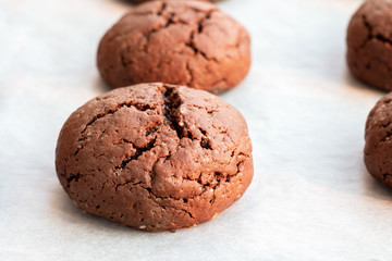 Baked cracked round chocolate cookies on a baking sheet with parchment paper just taken out of the oven. Tea snack. Selective focus. Closeup view