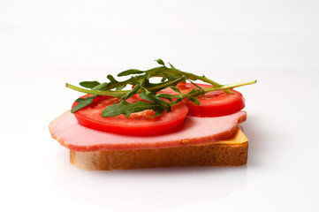 Sandwich made of balyk, cheese, bread, tomatoes and arugula on a white plate side view