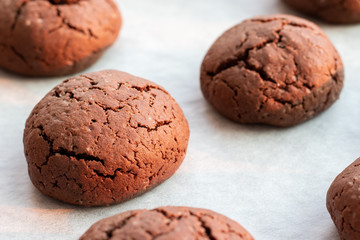 Baked cracked round chocolate cookies on a baking sheet with parchment paper just taken out of the oven. Tea snack. Selective focus. Closeup view